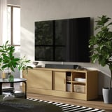 Large tv stand TONSTAD with smooth wooden finish, featuring sliding doors and open shelves, positioned against a wall with a flat screen tv on top.