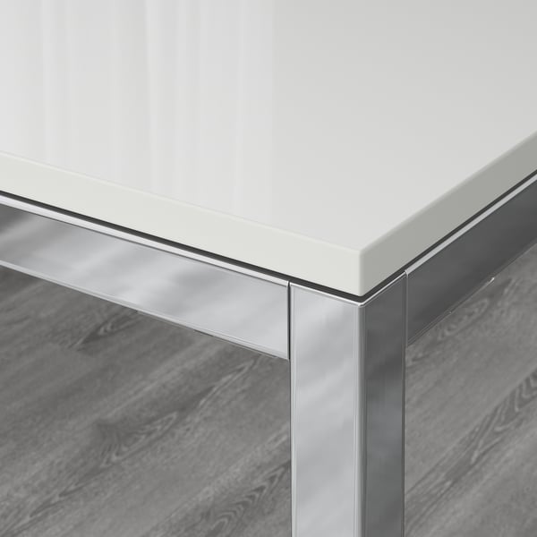 Modern dining table corner, sleek glossy white top and sturdy chrome frame, reflecting light and smooth finish.