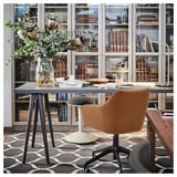 Home office with TOSSBERG chair, leather brown, glass desk, bookshelves filled with books, patterned rug, grey office accessories.