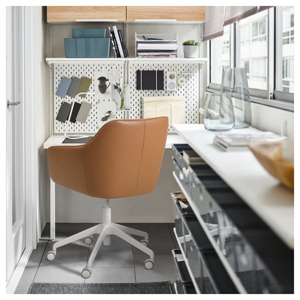 Home office setup with TOSSBERG brown leather swivel chair, white desk, pegboard, and shelves against window.