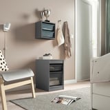 Modern teens room with TROFAST grey storage units, cushioned chairs, and hanging textiles. Heater and books visible, light-colored flooring.