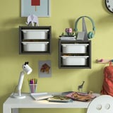 Black TROFAST wall boxes store items above a white desk with lamp, books, backpack, and toy giraffe.