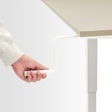 Hand adjusts TROTTEN desk crank, promoting ergonomic standing.
