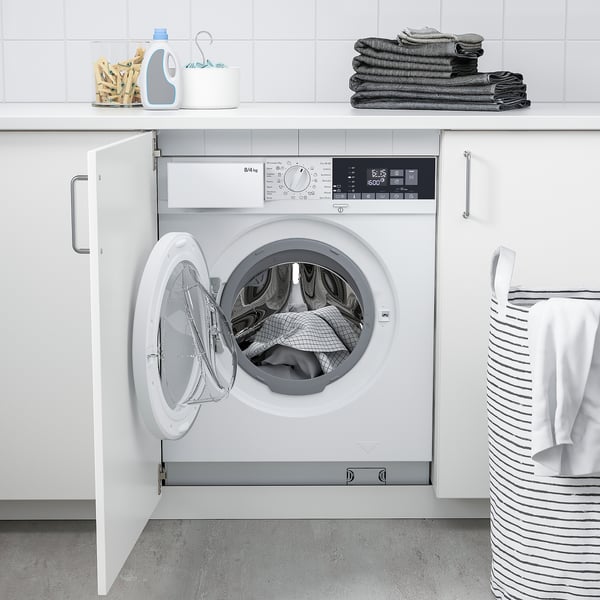 White 2-in-1 washer/dryer behind open cabinet, surrounded by towels & supplies, with striped basket nearby.