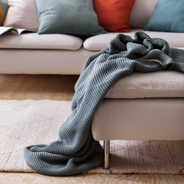 A cozy living room with a light grey sofa, adorned with a soft, gray knitted blanket casually draped over one arm.