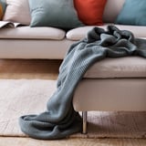 A cozy living room with a light grey sofa, adorned with a soft, gray knitted blanket casually draped over one arm.