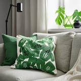 Underbloomma cushion in green/white on gray sofa with green pillows, lamp, and plant.