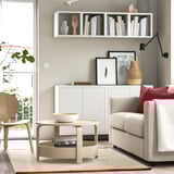 Modern living room with gray sofa, red pillows, coffee table, books, and wall shelf.