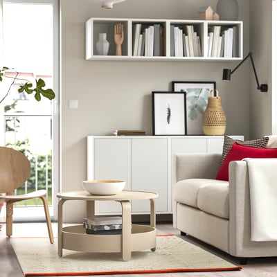 Modern living room with gray sofa, red pillows, coffee table, books, and wall shelf.
