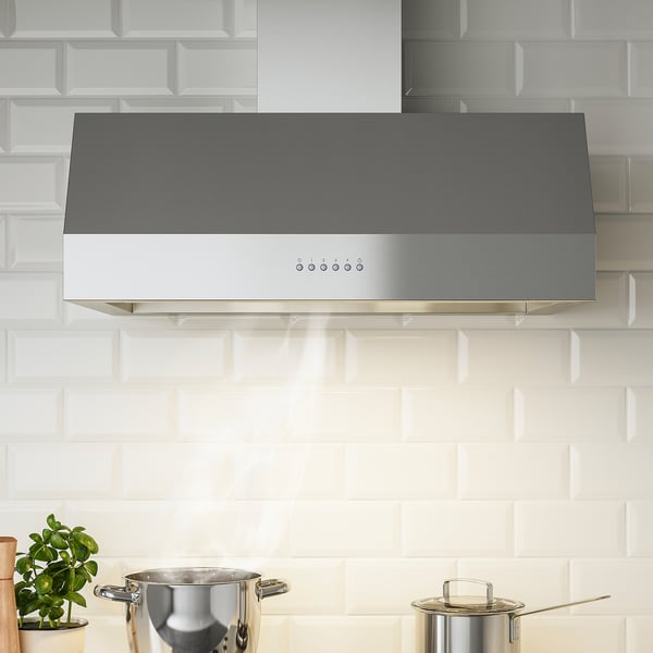 Modern stainless steel kitchen range hood installed above a cooktop, featuring led lights and control panel with three speeds and booster function.