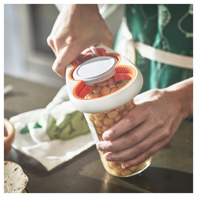 Two hands using an orange and white UPPFYLLD jar opener to twist off a lid from a glass jar filled with chickpeas.