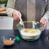 Person is adding spices from a small bowl into a large mixing bowl using measuring spoons from the UPPFYLLD set.