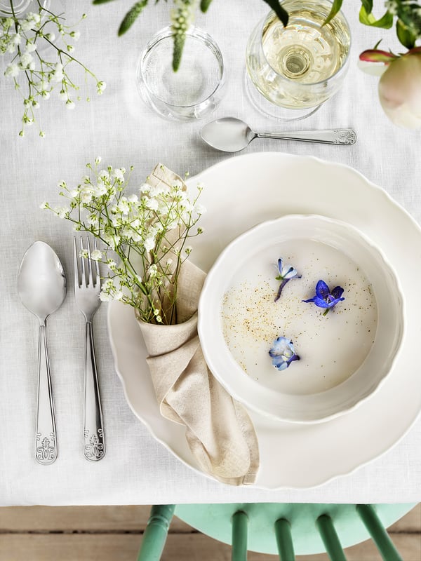 A rustic white porcelain bowl with blue flowers sits on a white tablecloth beside silverware.