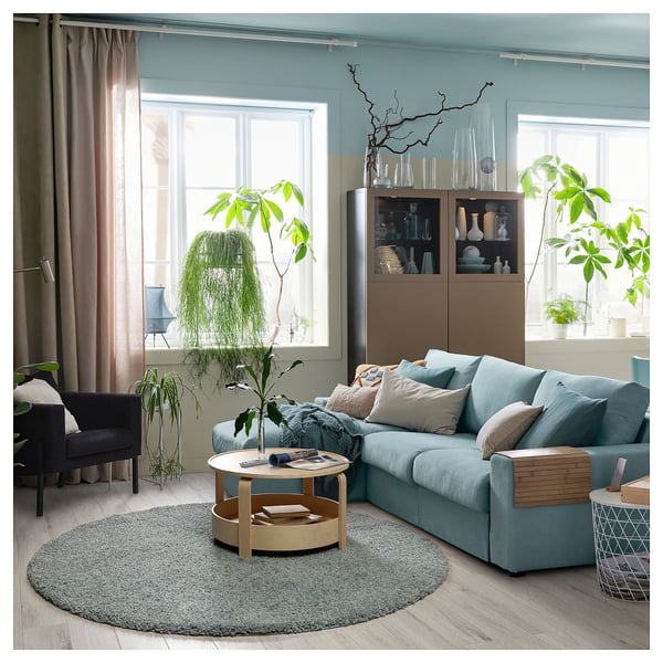 Modern living room with blue furniture, grey rug, wooden coffee table, plants, and large window.