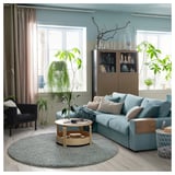 Modern living room with blue furniture, grey rug, wooden coffee table, plants, and large window.