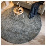 A round, grey UTREDNING area rug on a wooden floor, with a side table and couch nearby. The rug has a soft, shaggy texture.