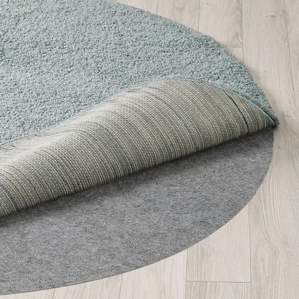 Round rug with soft, thick pile, showing quality texture and design, partially folded on light wooden floor.