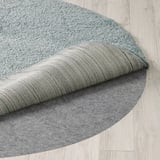 Round rug with soft, thick pile, showing quality texture and design, partially folded on light wooden floor.