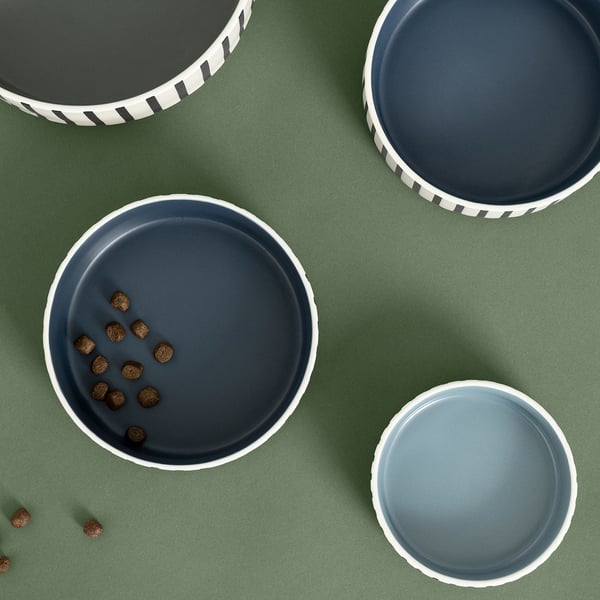 Three dark blue stoneware pet bowls on green surface. One filled with brown pet food. Simple design with white accents, suitable for modern homes.