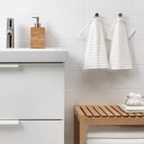 Modern bathroom with VÅGSJÖN towels on hooks, wooden towel rack, and soap dispenser beside chrome faucet.