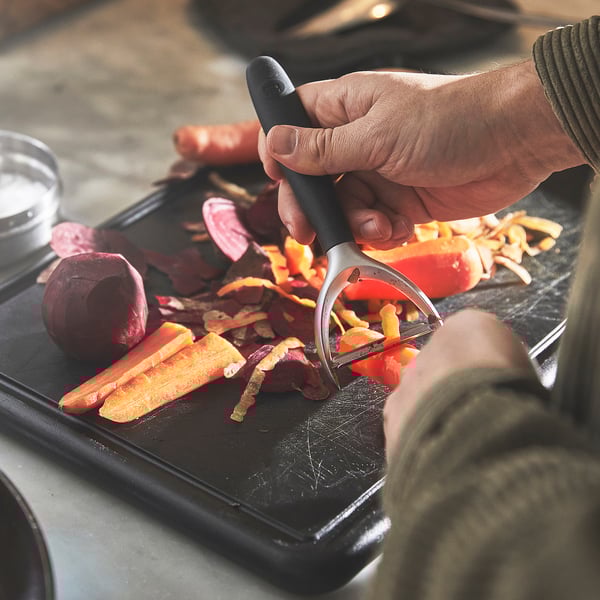 A person peels vegetables using a peeler over a cutting board, demonstrating the tools efficiency in preparing food.