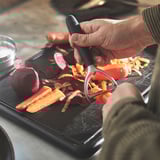 A person peels vegetables using a peeler over a cutting board, demonstrating the tools efficiency in preparing food.