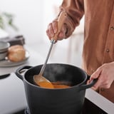 Cook stirs orange soup with steam and bread.