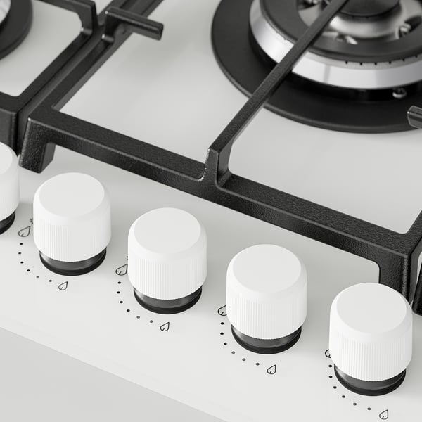Gas hob close-up. Sleek glass surface, five knobs, sturdy cast iron supports.