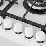 Gas hob close-up. Sleek glass surface, five knobs, sturdy cast iron supports.