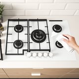 Cleaning VASASTAN gas hob with 5 burners, cast iron supports, electronic ignition, easy-clean surface.