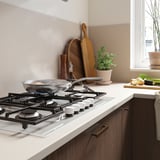 Clean modern kitchen with white gas stove, wood accents, and fresh ingredients near window.