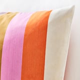 Decorative cushion with vibrant horizontal stripes in pink, orange, gold, and white, soft iridescent fabric.