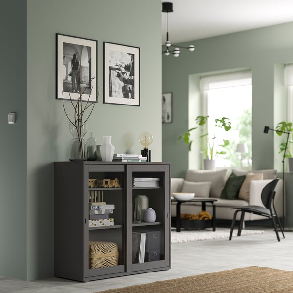 Modern mint living room with VIHALS black cabinet, gray couch, and large windows with plants.