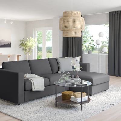 Modern living room with grey sectional sofa, large soft mattress, white pillows, glass coffee table, and large pendant lamp.