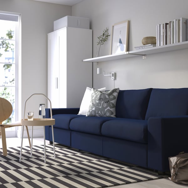 Modern living room with blue VIMLE sofa, white decor, black & white striped rug, and white cabinet. Sofa pillows included.