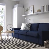 Modern living room with blue VIMLE sofa, white decor, black & white striped rug, and white cabinet. Sofa pillows included.