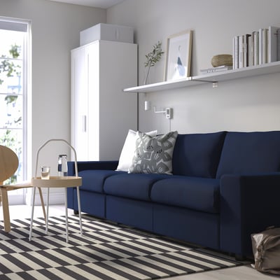 Modern living room with blue VIMLE sofa, white decor, black & white striped rug, and white cabinet. Sofa pillows included.