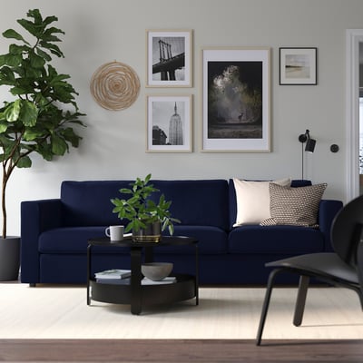 Cozy living room with navy VIMLE sofa, beige cushions, black coffee table, and minimalist art. Large houseplant adds greenery.