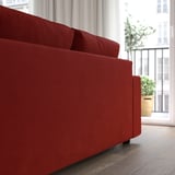 Bright red sofa with chaise, versatile seating. Modern design, large cushions. Near window with green plant, urban view.