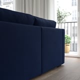 Dark blue sofa with a chaise longue on the right, positioned near a large window with white curtains, offering a cozy and modern living room ambiance.