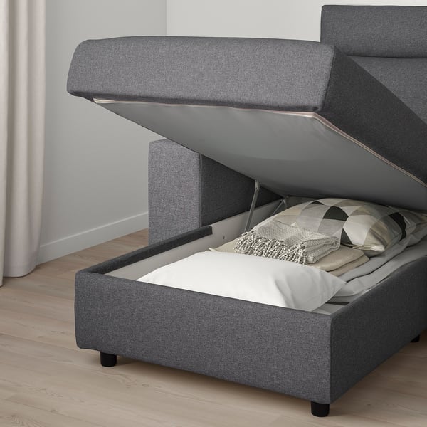 Gray upholstered sofa with open storage compartment under seat, revealing soft blankets and pillows.