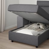 Gray upholstered sofa with open storage compartment under seat, revealing soft blankets and pillows.