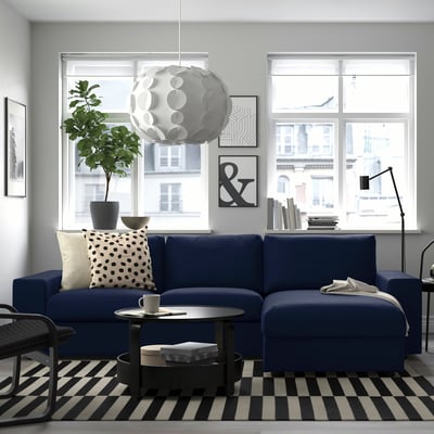 Modern living room with blue sectional sofa, large windows, black & white decor, hanging lamp, and striped rug.