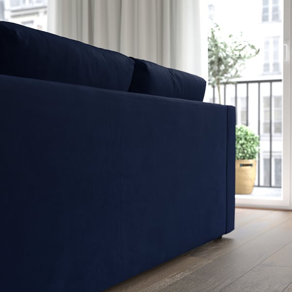 Blue velvet sofa near large window with curtain, offering comfort and modern style.