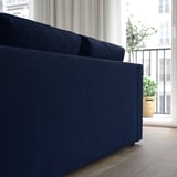 Blue velvet sofa near large window with curtain, offering comfort and modern style.