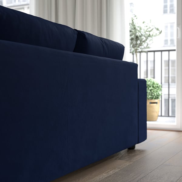 Modern navy sofa with chaise, near large windows and a potted plant.