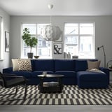 Modern living room with large blue VIMLE sectional sofa, stripe rug, black coffee table, unique pendant light, and city view.