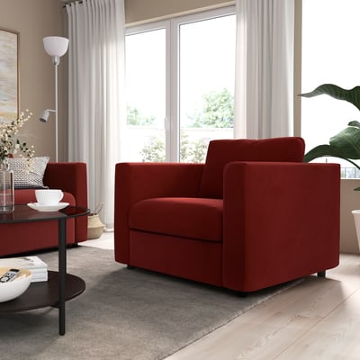 Modern living room with two red VIMLE armchairs, cushions, side tables, and large window. Soft lighting, and a gray area rug. Cozy and stylish.