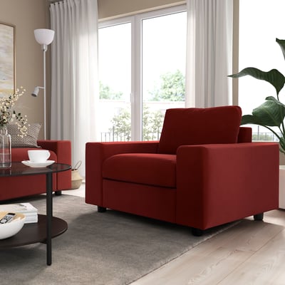 Bright red VIMLE sofa chair in cozy living room, beside a dark table with a white coffee cup. Large window with curtains behind.