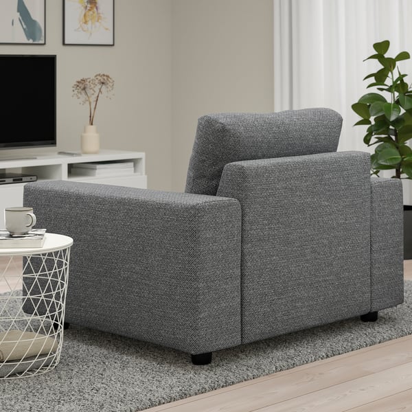 A cozy gray armchair in a living room, accompanied by a side table with a mug and a plant.